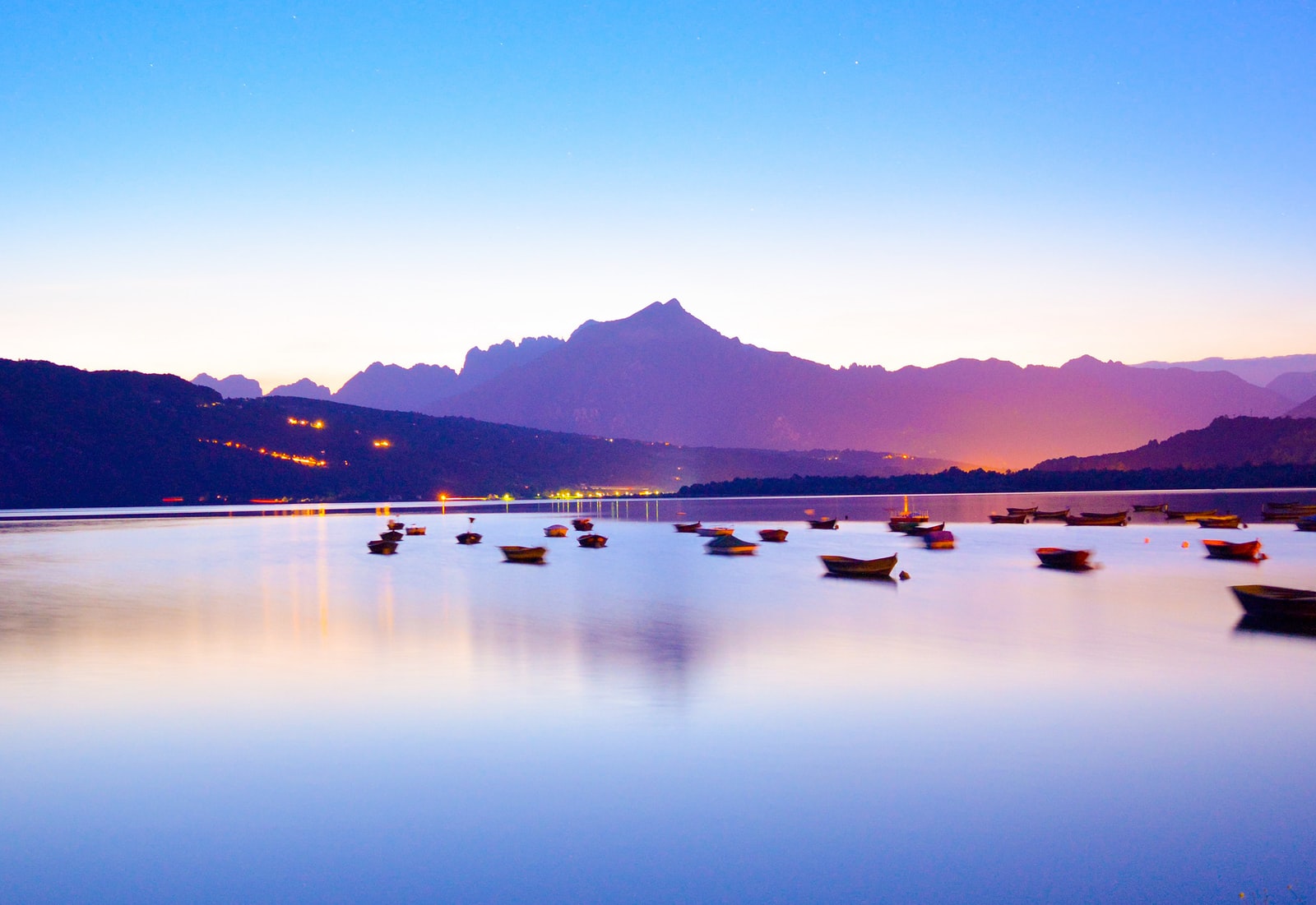 boats in body of calm water overlooking mountain and city lights